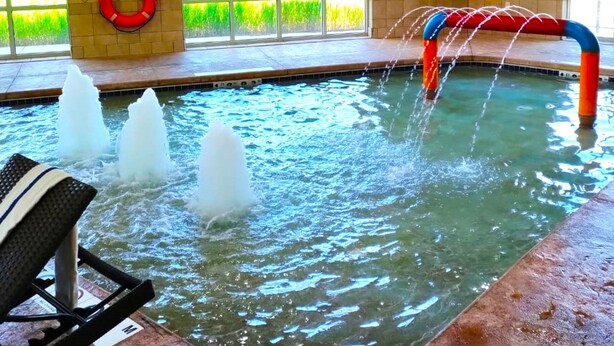 An indoor swimming pool with multiple water jets, a lifebuoy, and a bench. - Holiday Inn Express & Suites Milwaukee Nw Park Place by IHG (Milwaukee)