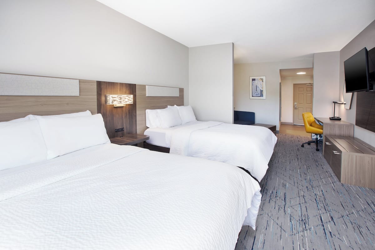 A hotel room with two beds, a desk, a chair, a TV, and a door leading to another room.