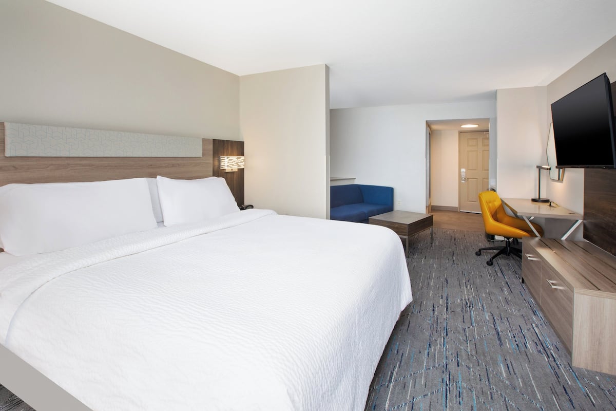 A hotel room with a large bed, a desk with a chair, a flat-screen TV, and a blue sofa.