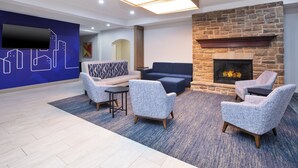 A modern lounge area with a stone fireplace, comfortable seating, and a cityscape mural on the wall. - Holiday Inn Express & Suites Milwaukee Nw Park Place by IHG (Milwaukee)