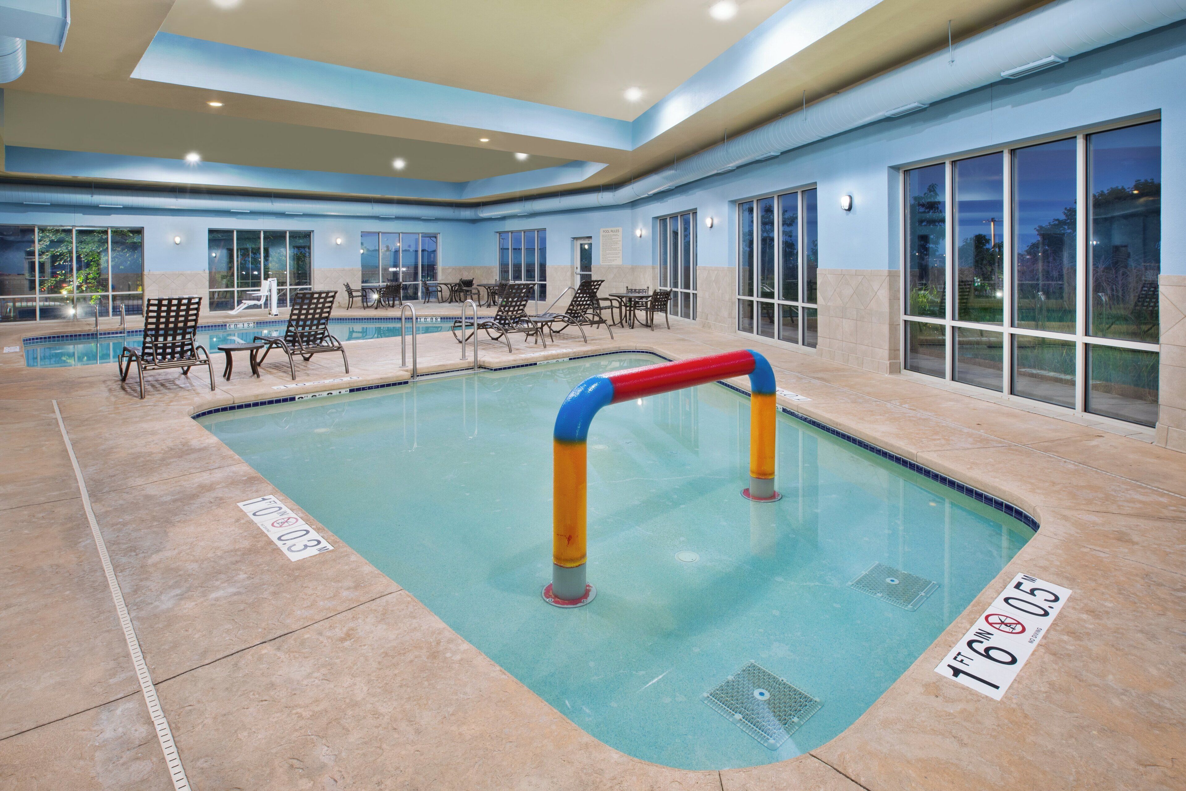 An indoor swimming pool with clear water, marked depth lines, and a pool ladder.