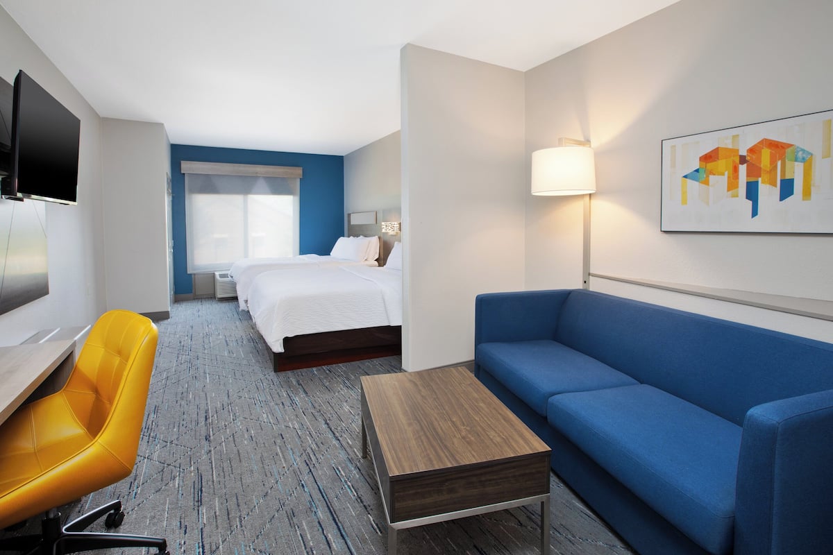 A hotel room with a bed, a blue sofa, a yellow chair, a TV, and a lamp.