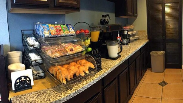 A kitchen counter with a breakfast bar, including a glass display case with pastries, a coffee maker, and a fruit bowl. - Escondido Lodge (Escondido)