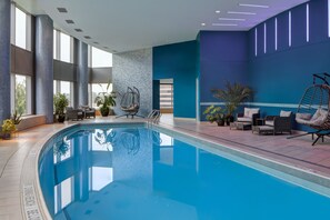 A swimming pool with lounge chairs and a hanging chair, surrounded by large windows and potted plants. - JW Marriott Hotel Grand Rapids (Grand Rapids)