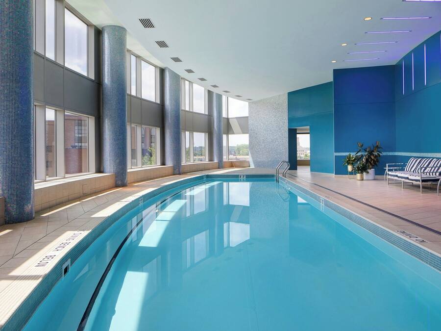 Una piscina interior amb aigua blava cristal·lina, grans finestres i una zona de solàrium amb gandules.