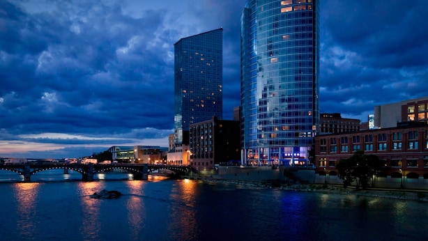 Un hôtel moderne à la façade en verre, situé près d’une rivière et d’un pont.