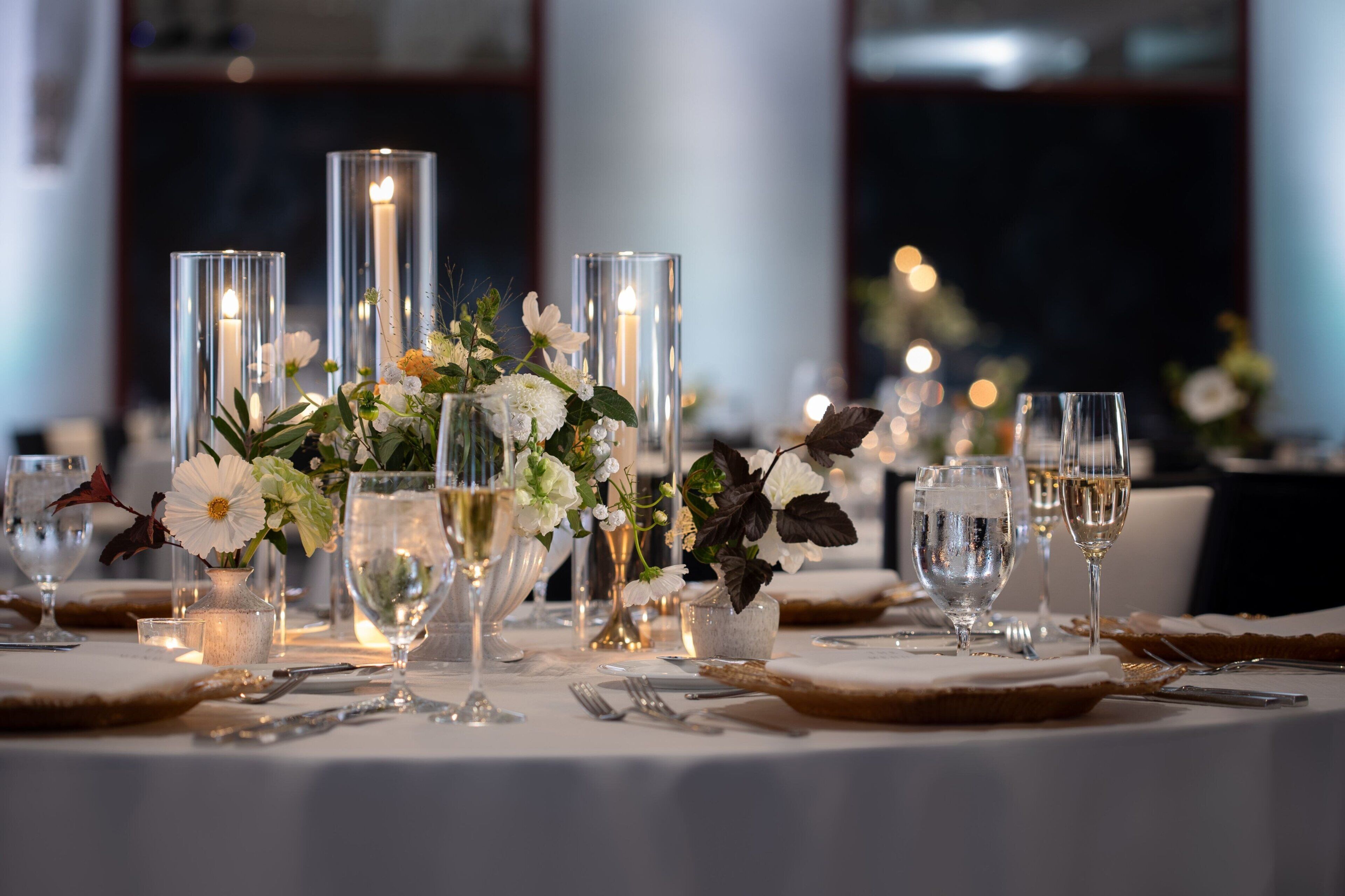 A table set for a formal dinner with tall glass vases, candles, and white flowers.
