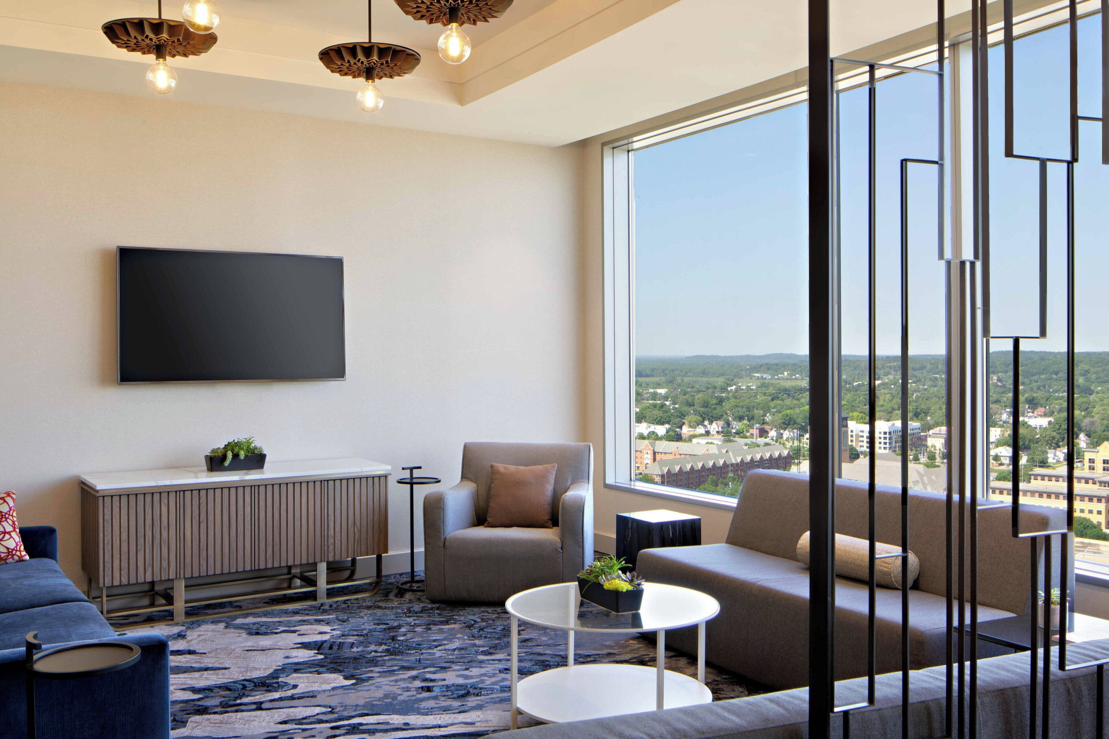 A modern living room with a large window, a flat-screen TV, and a view of a cityscape.
