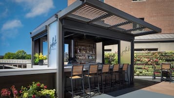 Un área de bar al aire libre con una sección de estar cubierta, una barra y una variedad de plantas y flores.