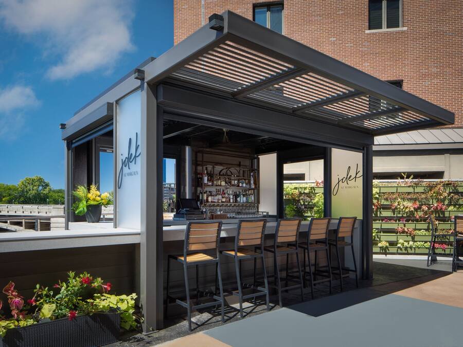Un área de bar al aire libre con una sección de estar cubierta, una barra y una variedad de plantas y flores.
