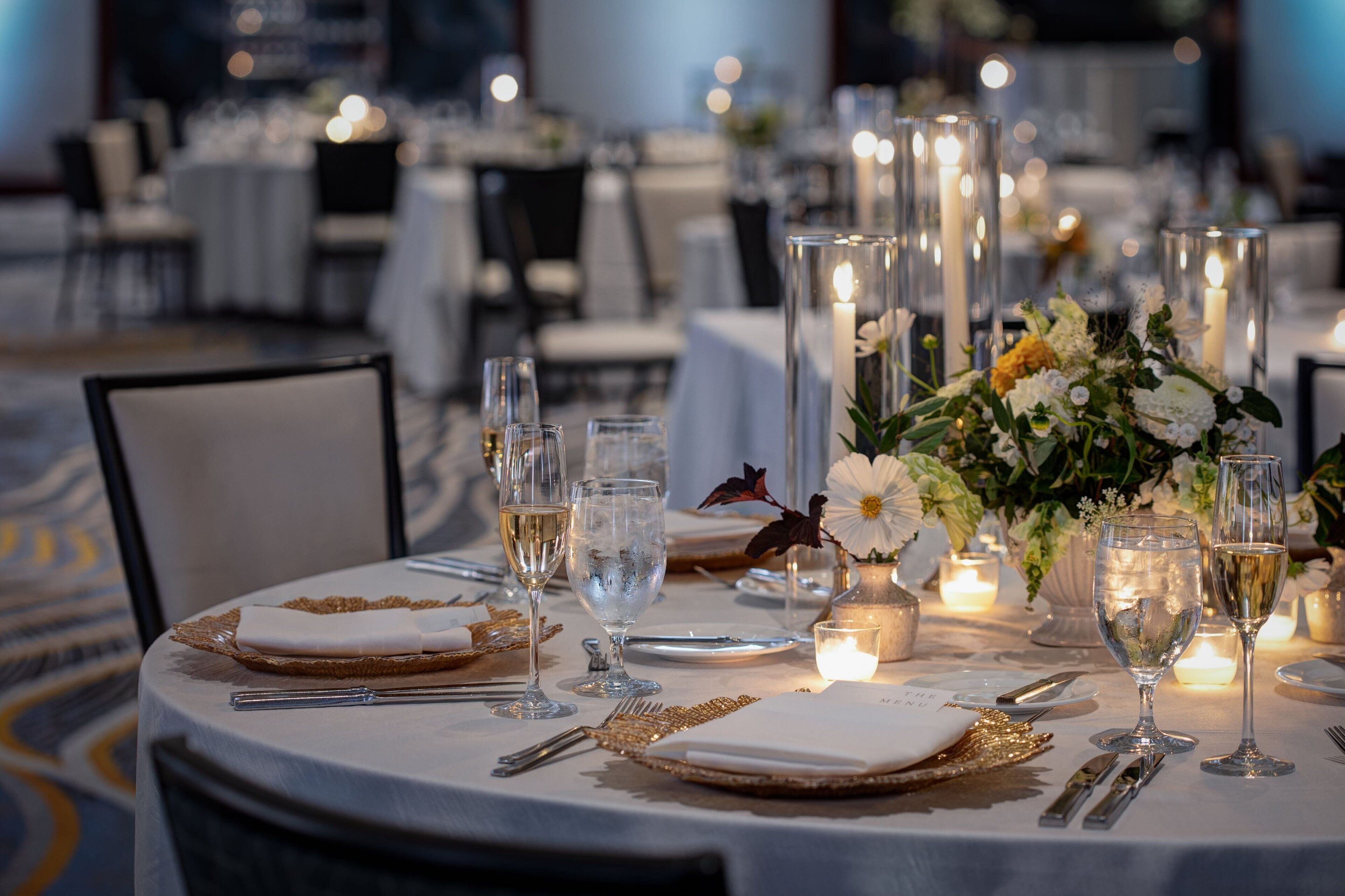 A well-set dining table with white tablecloths, gold cutlery, and clear glassware.