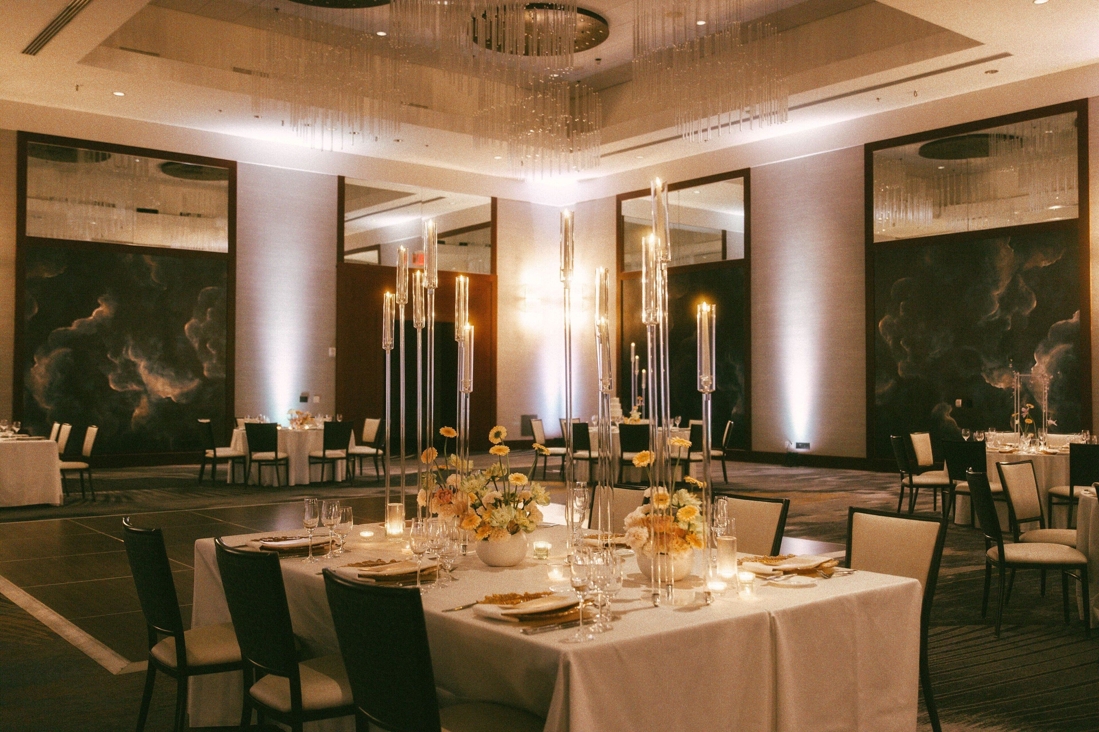 A banquet hall with tables set for dining, tall candles, and floral centerpieces.