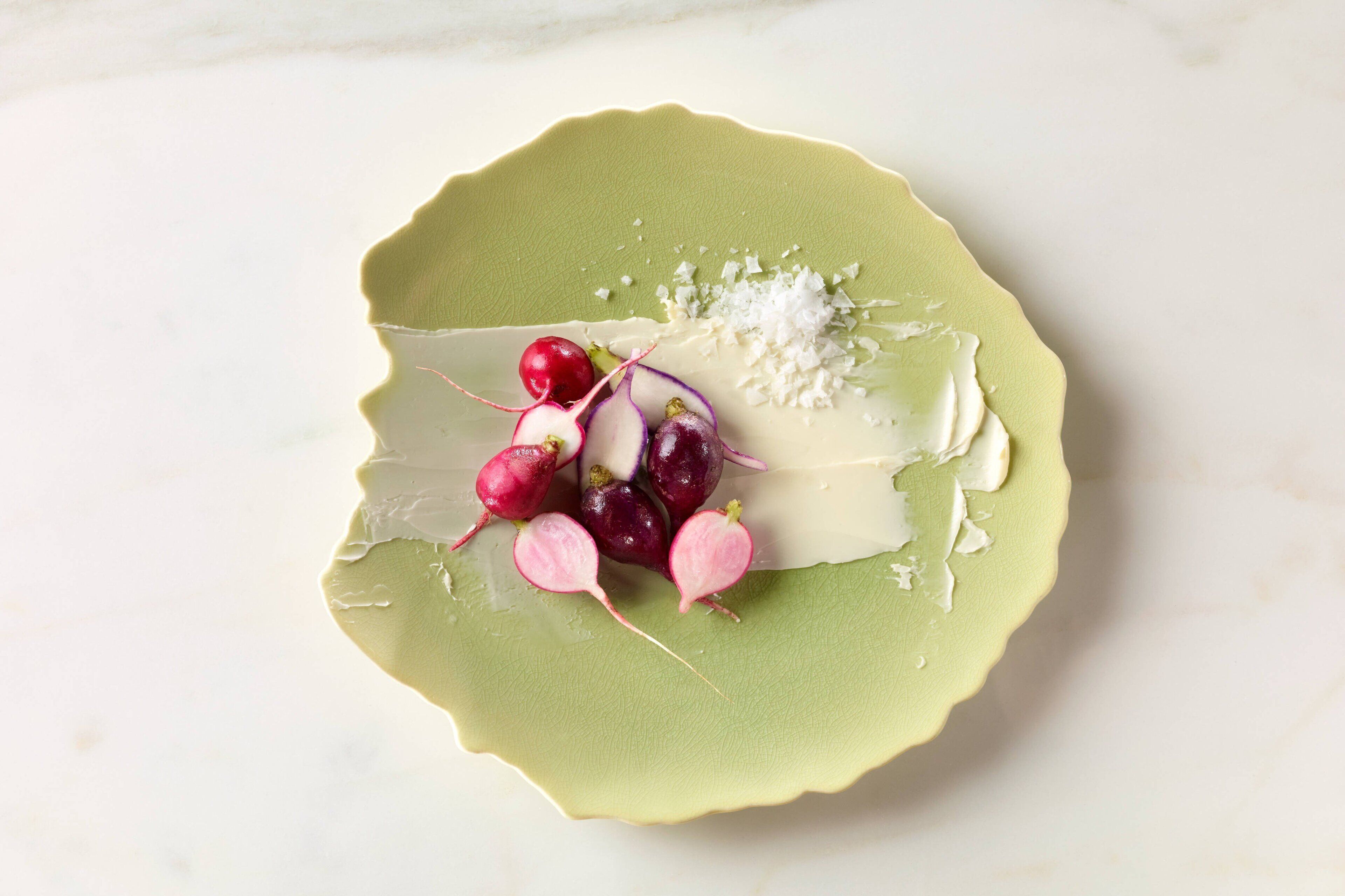 A green plate with radishes and a white creamy substance.