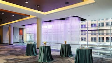 A spacious indoor area with three round tables covered with green tablecloths, each with a candle and a flower arrangement.