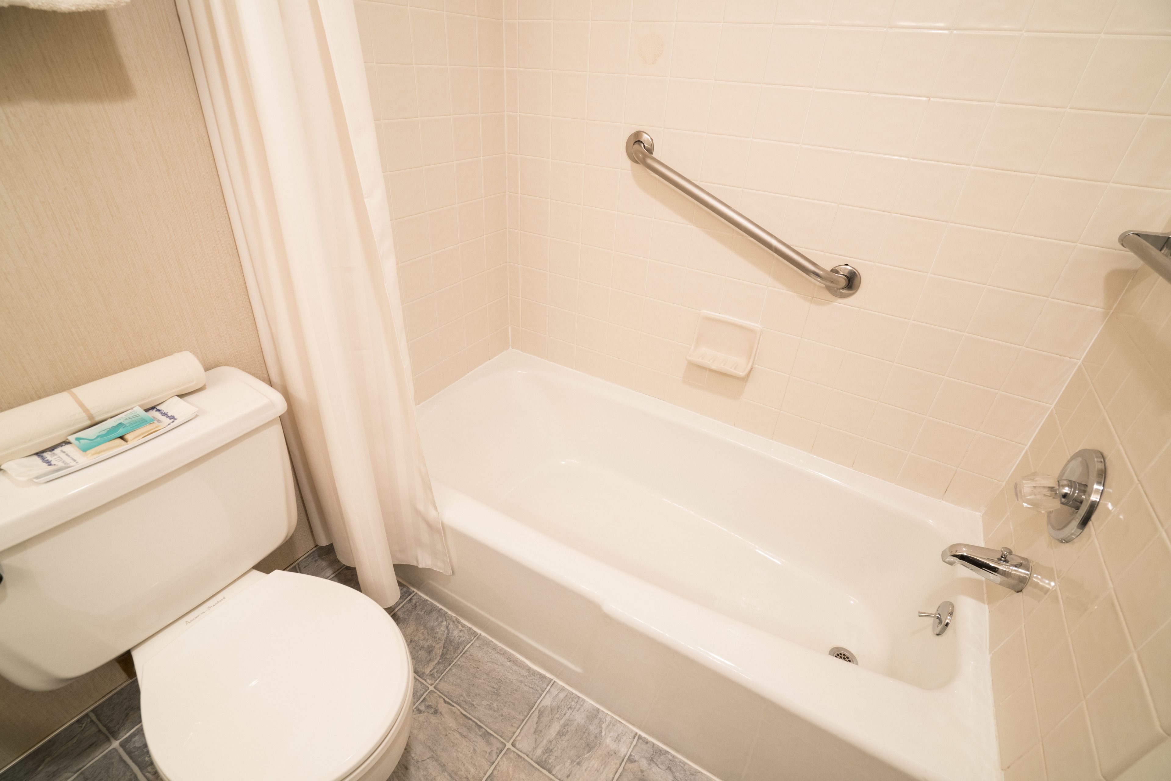 Ein Badezimmer mit einer weißen Badewanne, einer Toilette und einer Handstange.