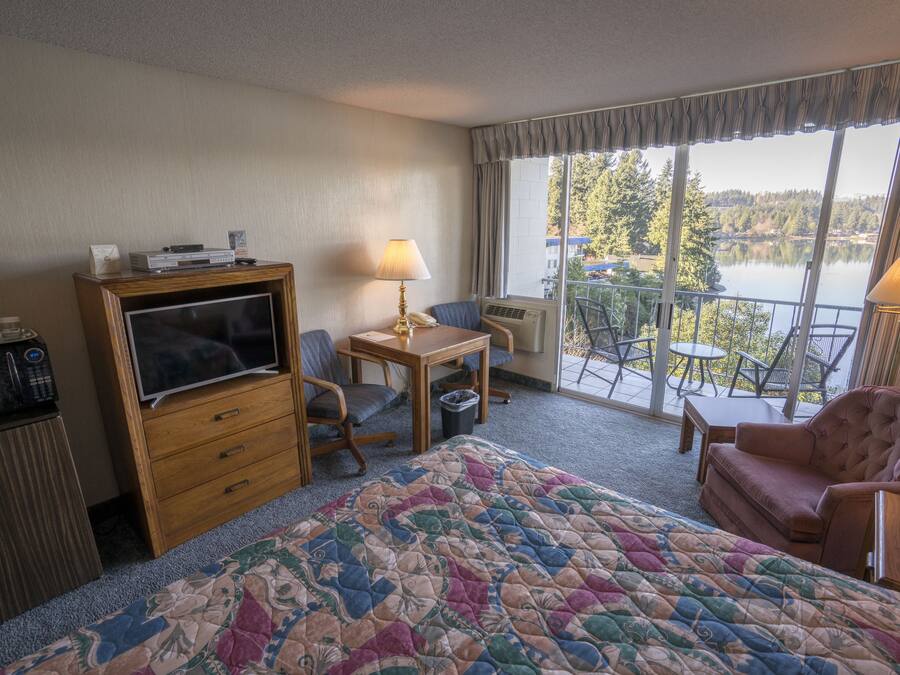 Habitación de hotel con cama, escritorio con lámpara, televisión y vista a un lago.