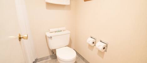 A small, clean bathroom with a toilet, two rolls of toilet paper, a towel rack with a towel, and a shower curtain.