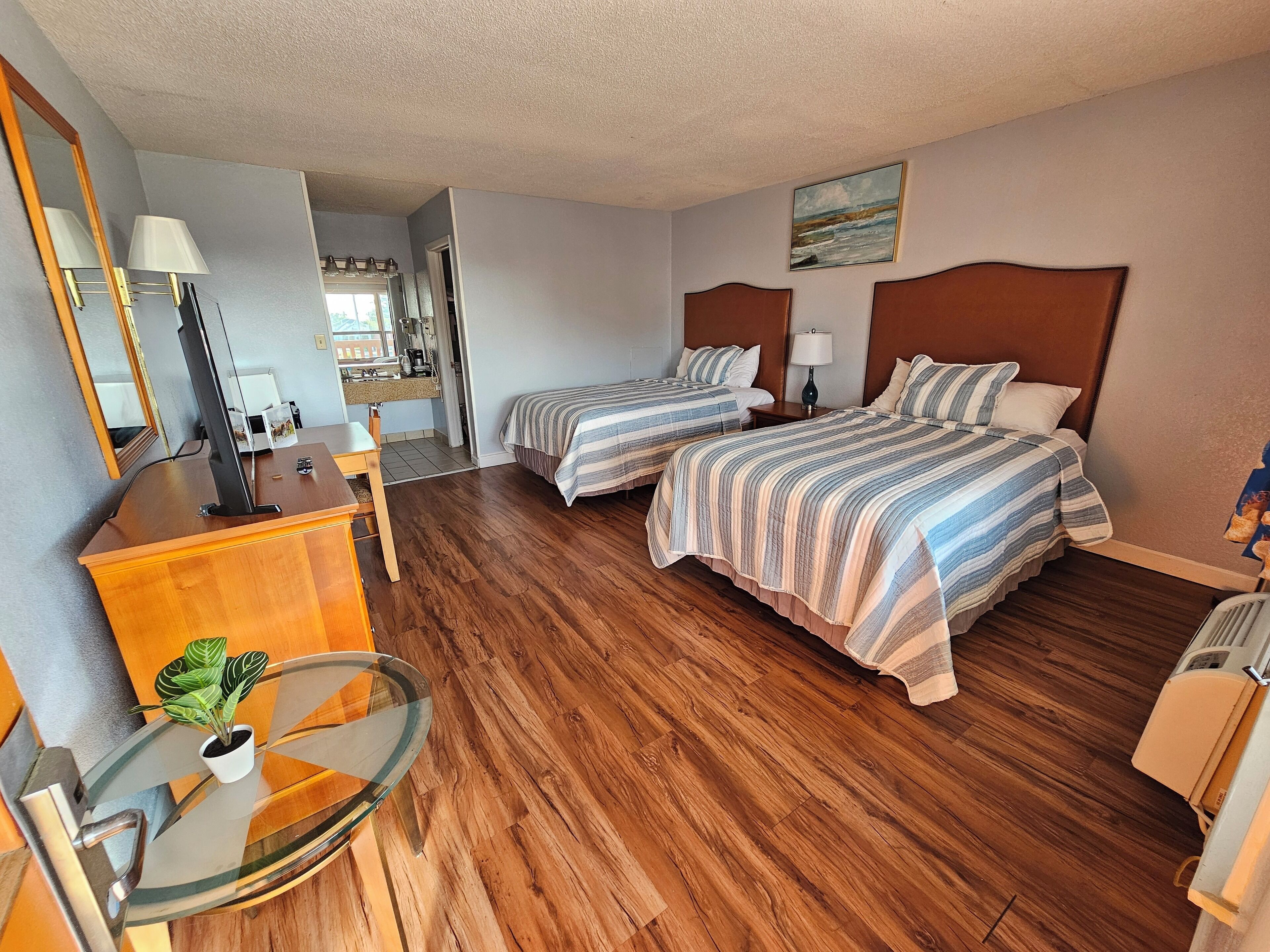 A hotel room with two beds, a desk, a chair, a small table with a plant, and a painting on the wall.