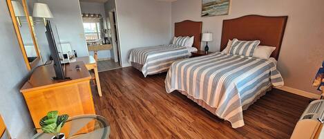 A hotel room with two beds, a desk, a chair, a small table with a plant, and a painting on the wall.