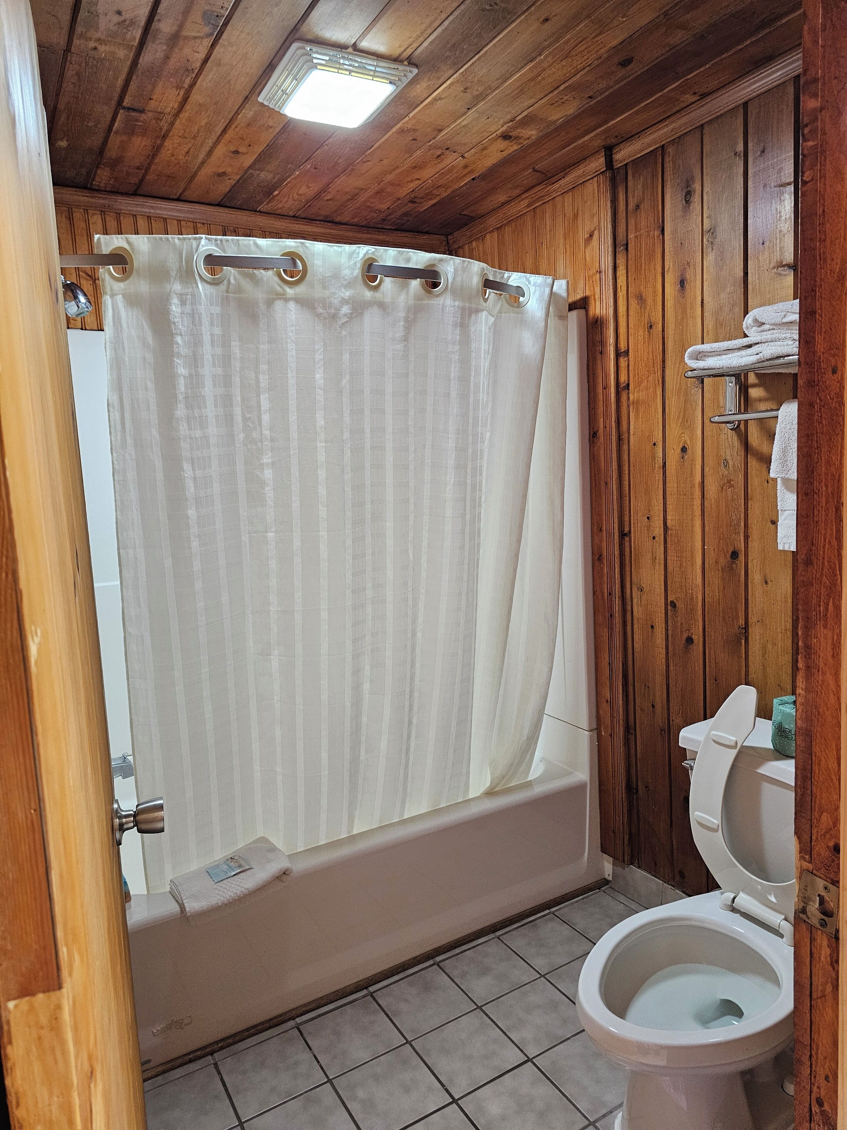 A bathroom with a wooden ceiling, a bathtub, a toilet, and a shower curtain.