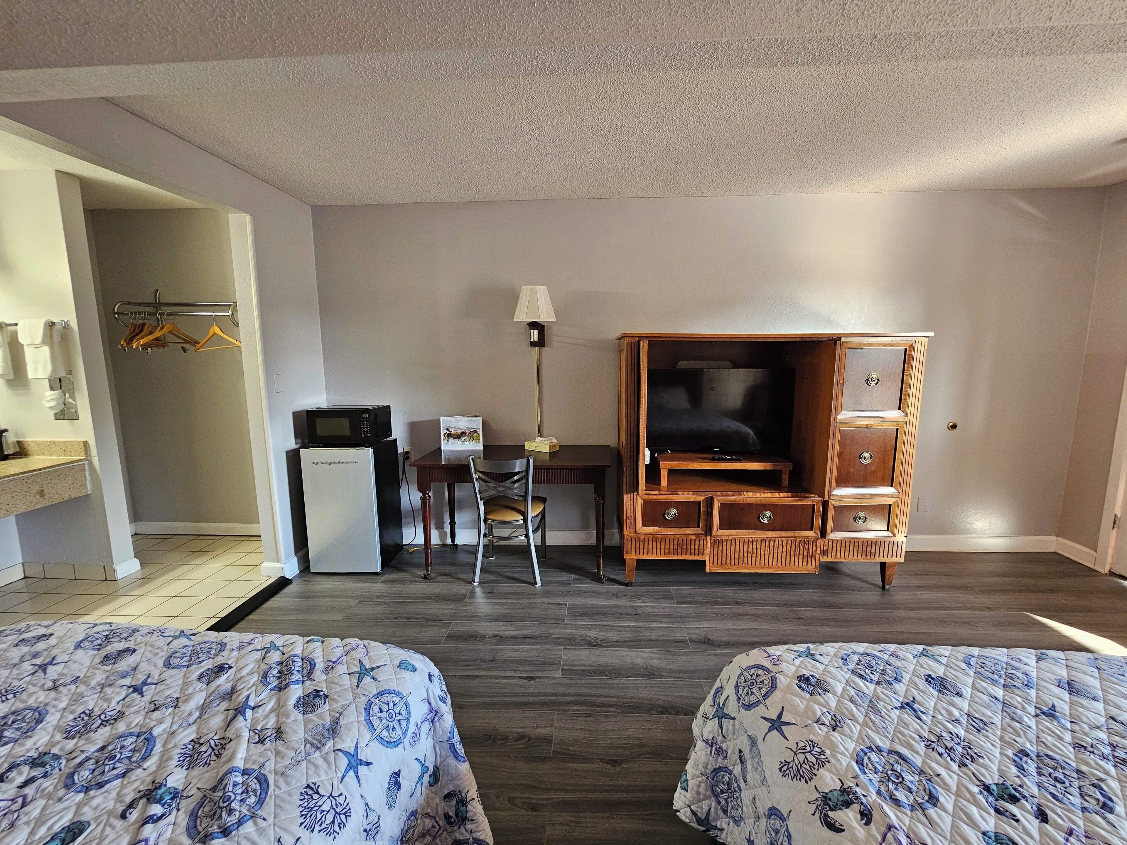 A hotel room with two beds, a desk with a computer, a TV, and a wardrobe.