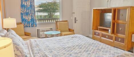 A hotel room with a bed, a chair, a small table, a TV cabinet, and a window with curtains.