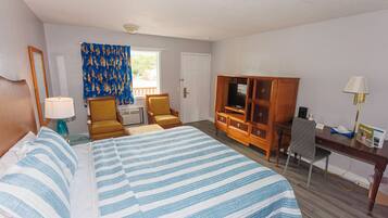 A hotel room with a bed, two chairs, a desk with a computer, a TV, and a window with curtains.