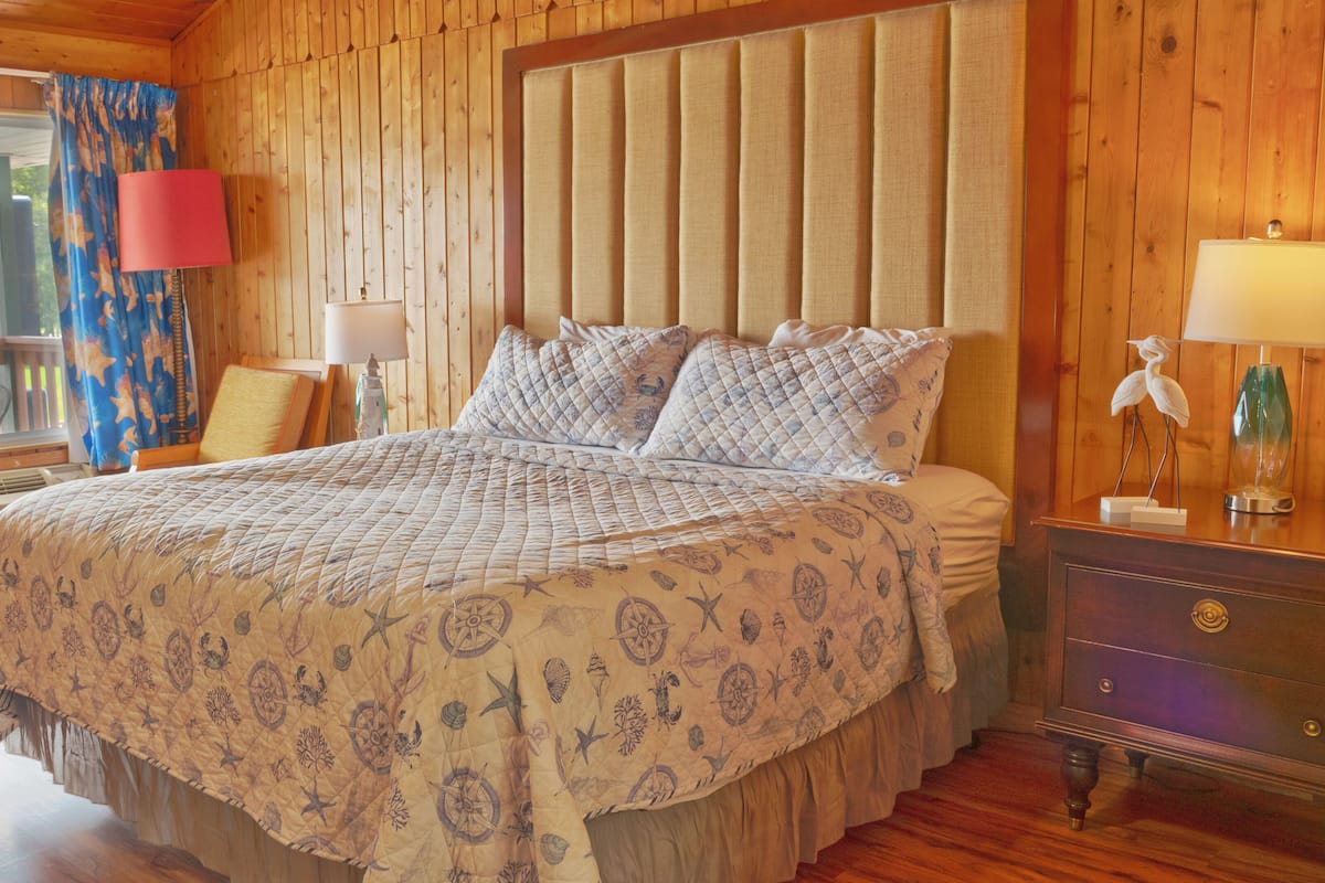 A wooden cabin-style bedroom with a large bed, a nightstand, and a window with curtains.