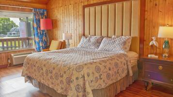 Un dormitorio tipo cabaña de madera con una cama grande, una mesita de noche y una ventana con cortinas.