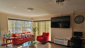A living room with a red sofa, a red armchair, a glass coffee table, and a TV mounted on the wall. - Atlantic Shores Inn and Suites (Chincoteague)