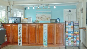 A reception desk with a 'WELCOME' sign, a 'Life is Better at the Beach' banner, and a display of travel brochures. - Atlantic Shores Inn and Suites (Chincoteague)