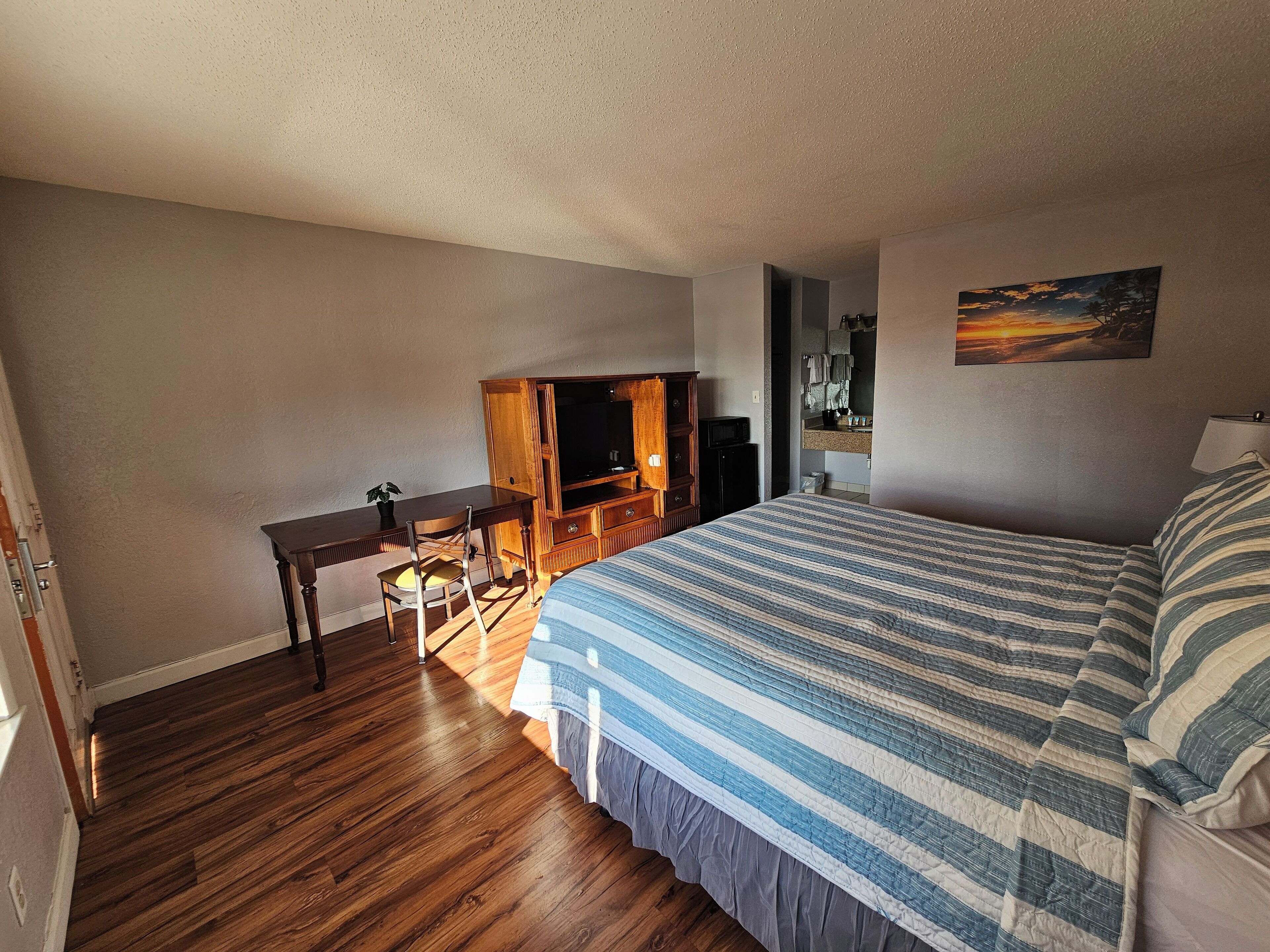 Un dormitorio con cama, escritorio, silla, televisor y un cuadro en la pared.