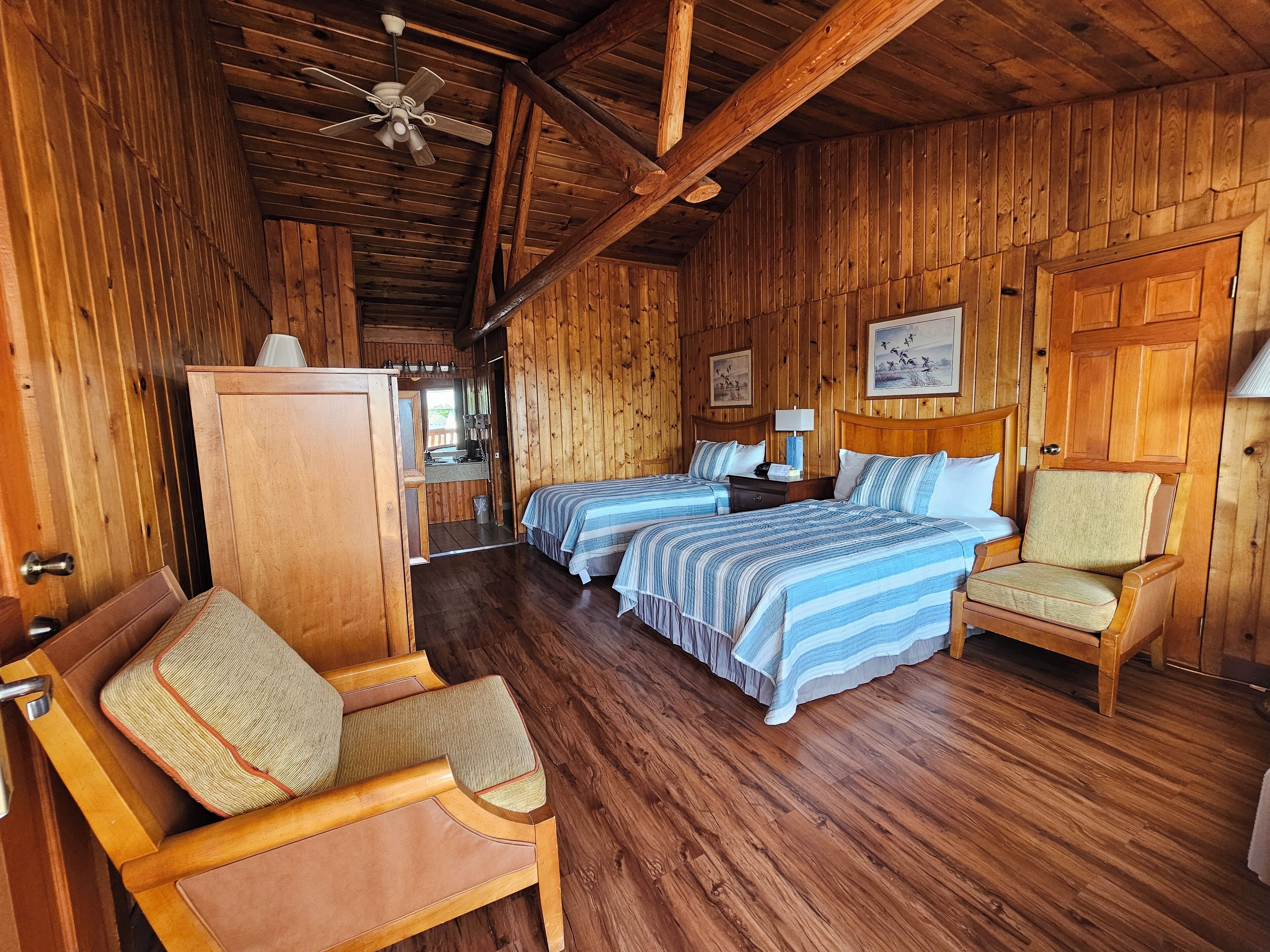 Une cabane en bois avec deux lits, une chaise, un bureau et un ventilateur de plafond.