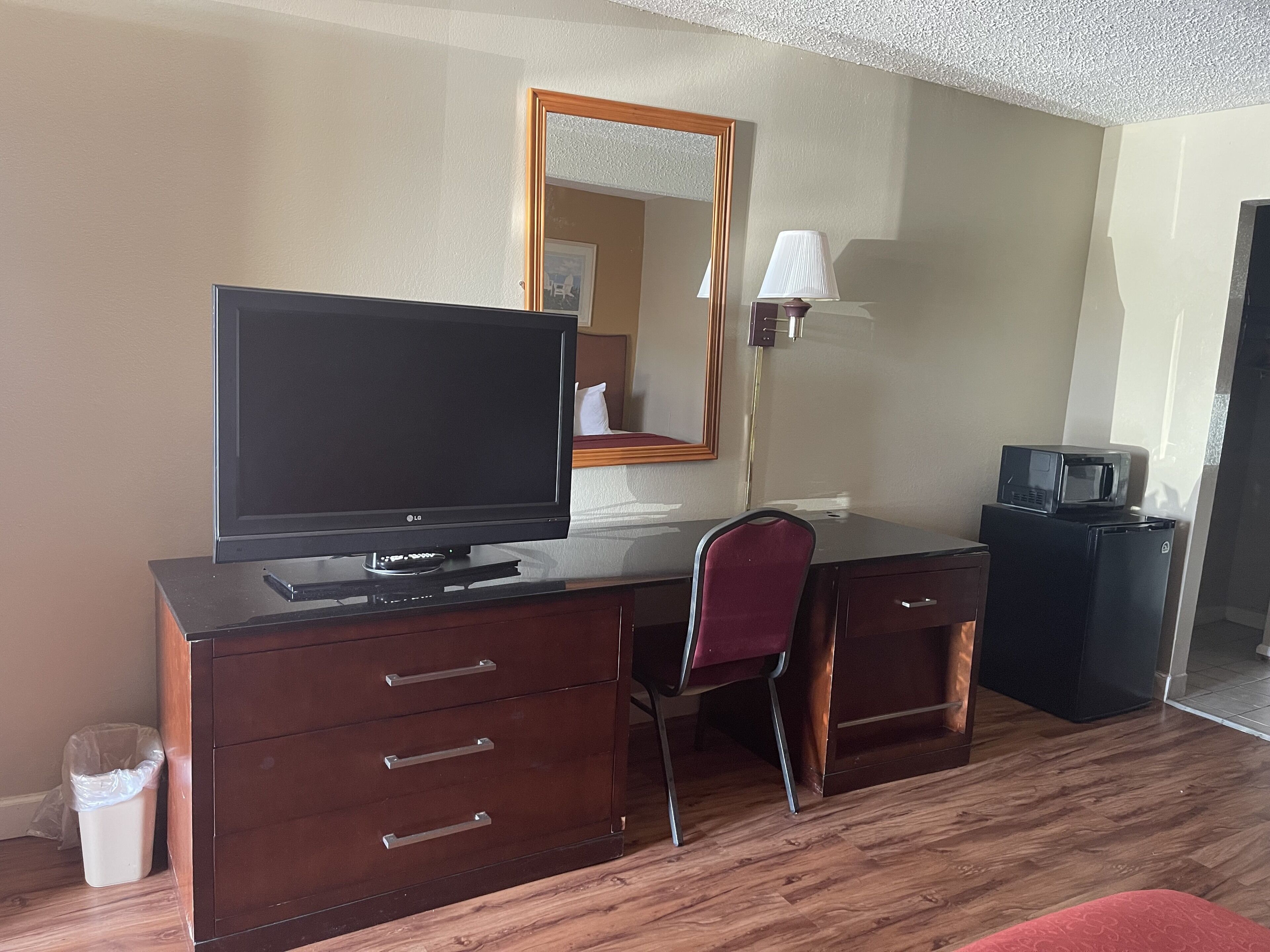 Una habitación de hotel con un escritorio de madera, televisor, una silla, lámpara y microondas.