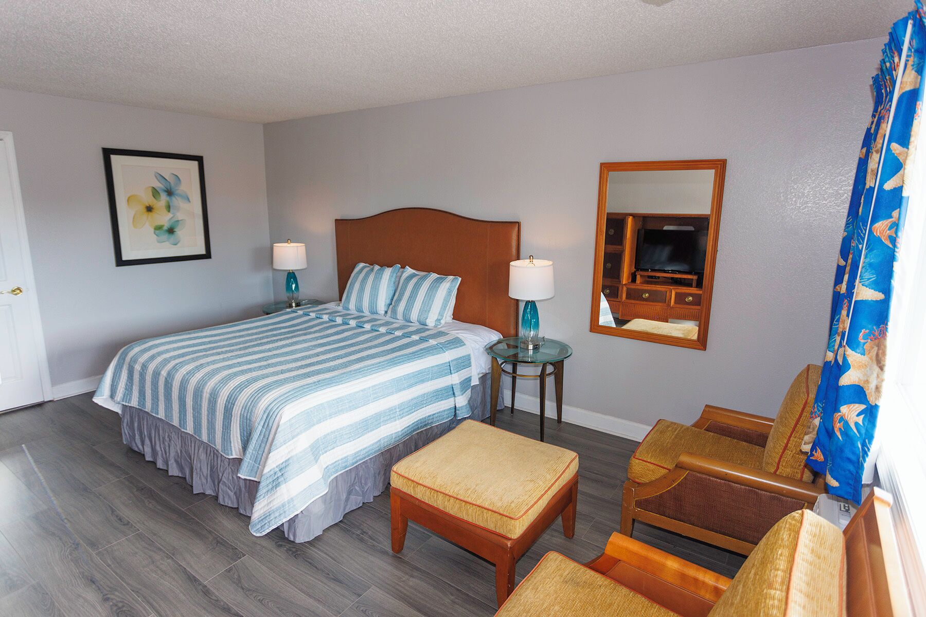 Une chambre d’hôtel avec un lit, une petite table avec une lampe, une chaise, un téléviseur et un tableau encadré au mur.