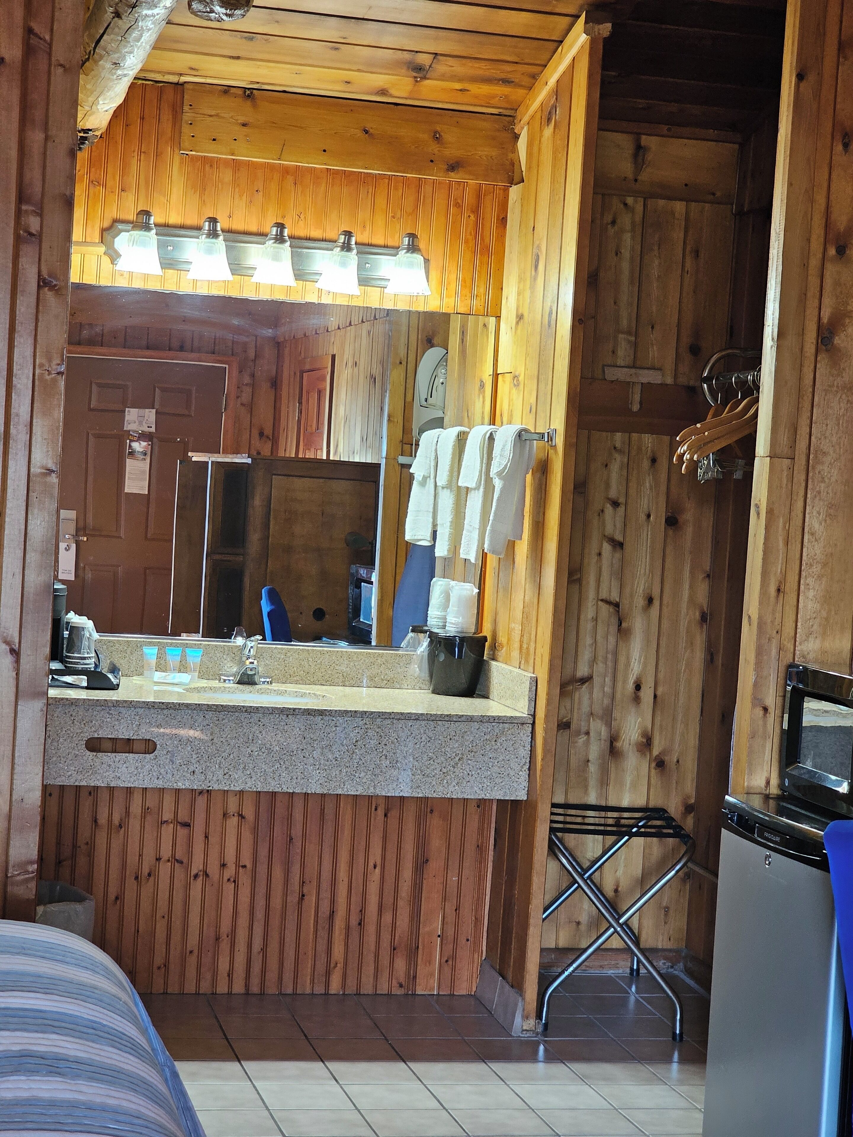 Interior de una cabaña de madera con kitchenette, un lavabo con espejo y un refrigerador pequeño.