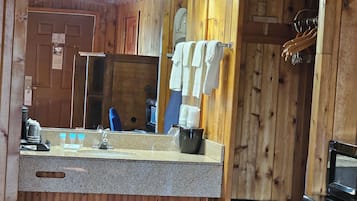 Interior de una cabaña de madera con kitchenette, un lavabo con espejo y un refrigerador pequeño.
