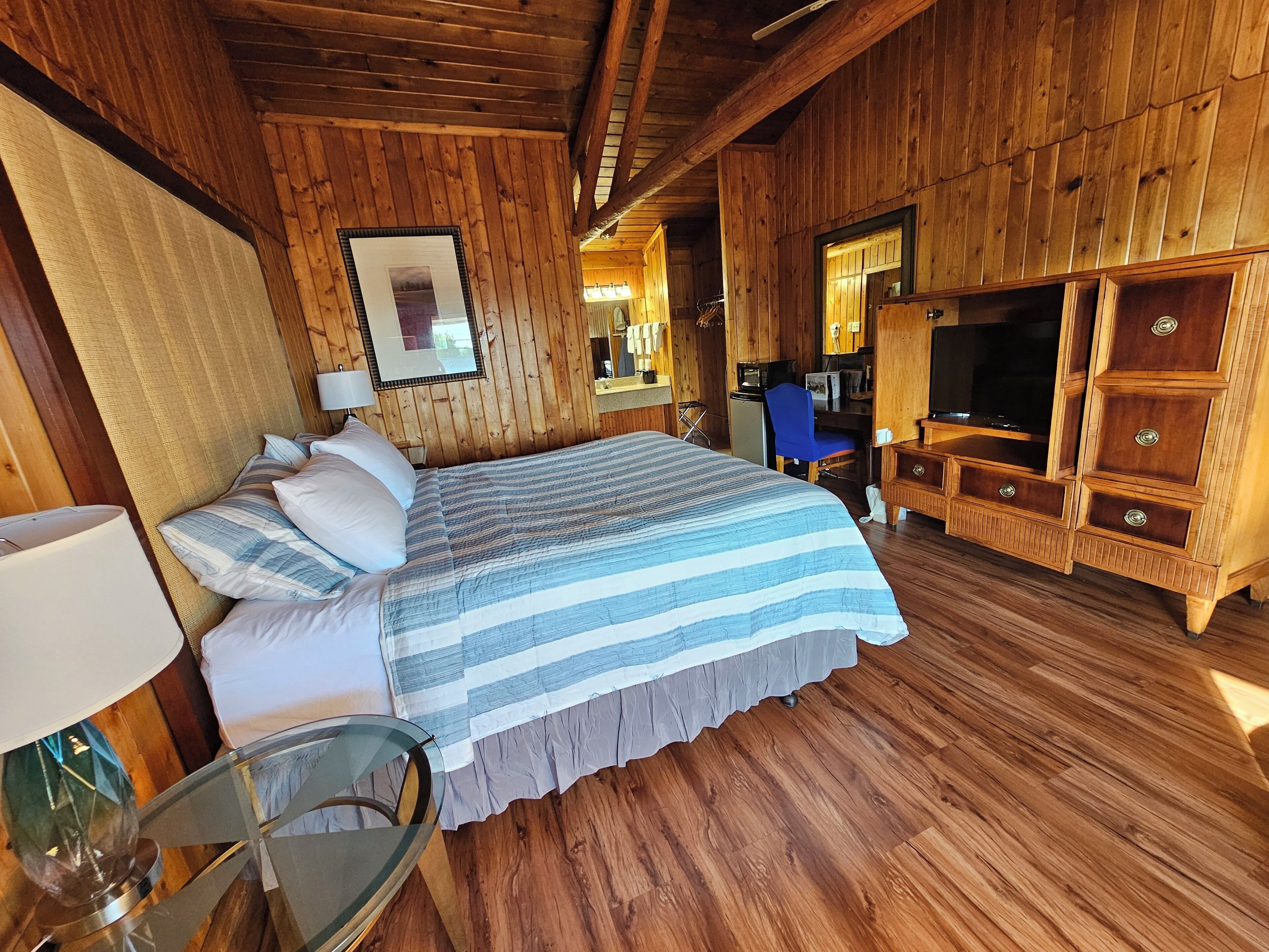 A wooden cabin room with a bed, a desk, a chair, and a TV.