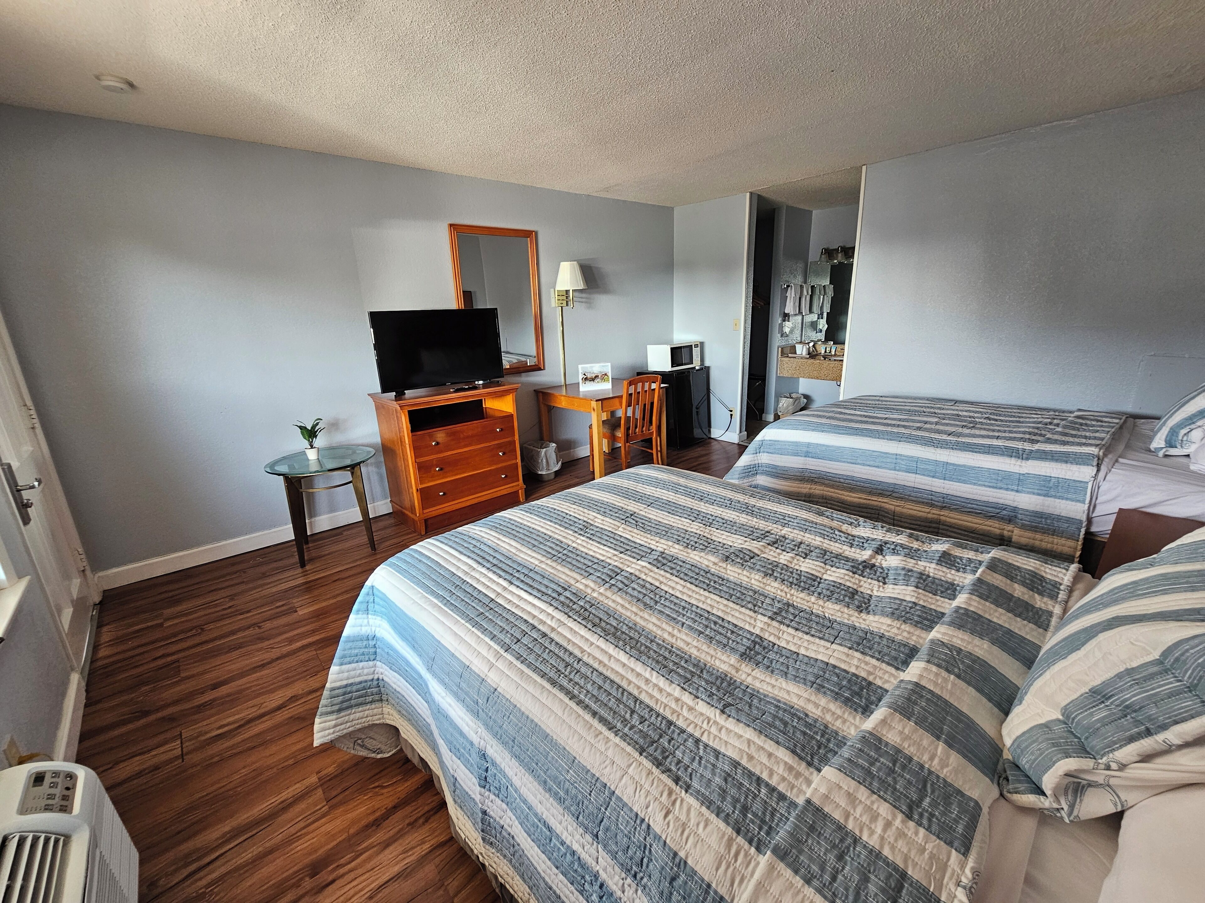 A hotel room with a bed, a desk with a computer, a television, and a mirror.