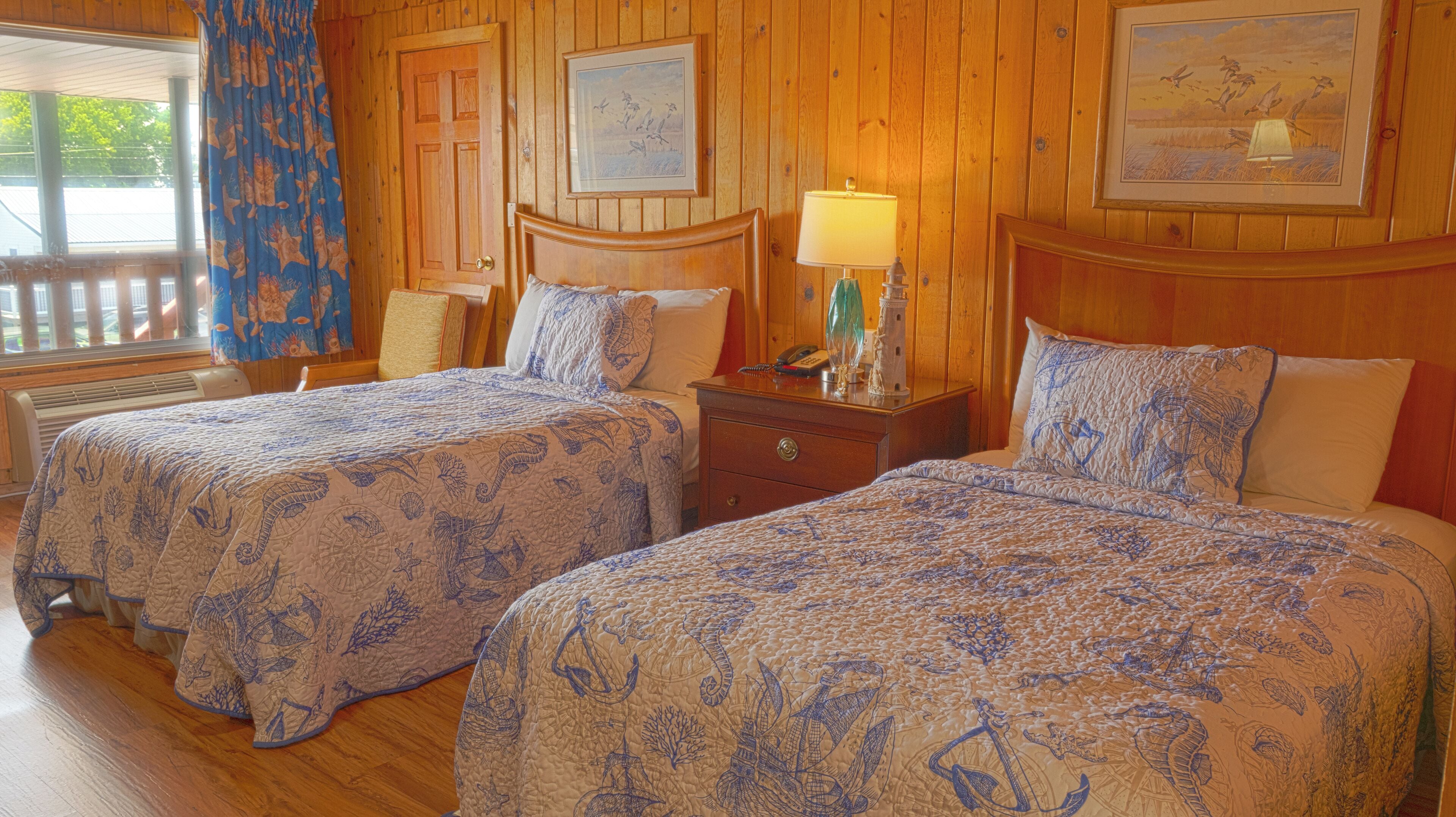 A room with two beds, wooden walls, and framed artwork.
