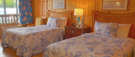 A room with two beds, wooden walls, and framed artwork.