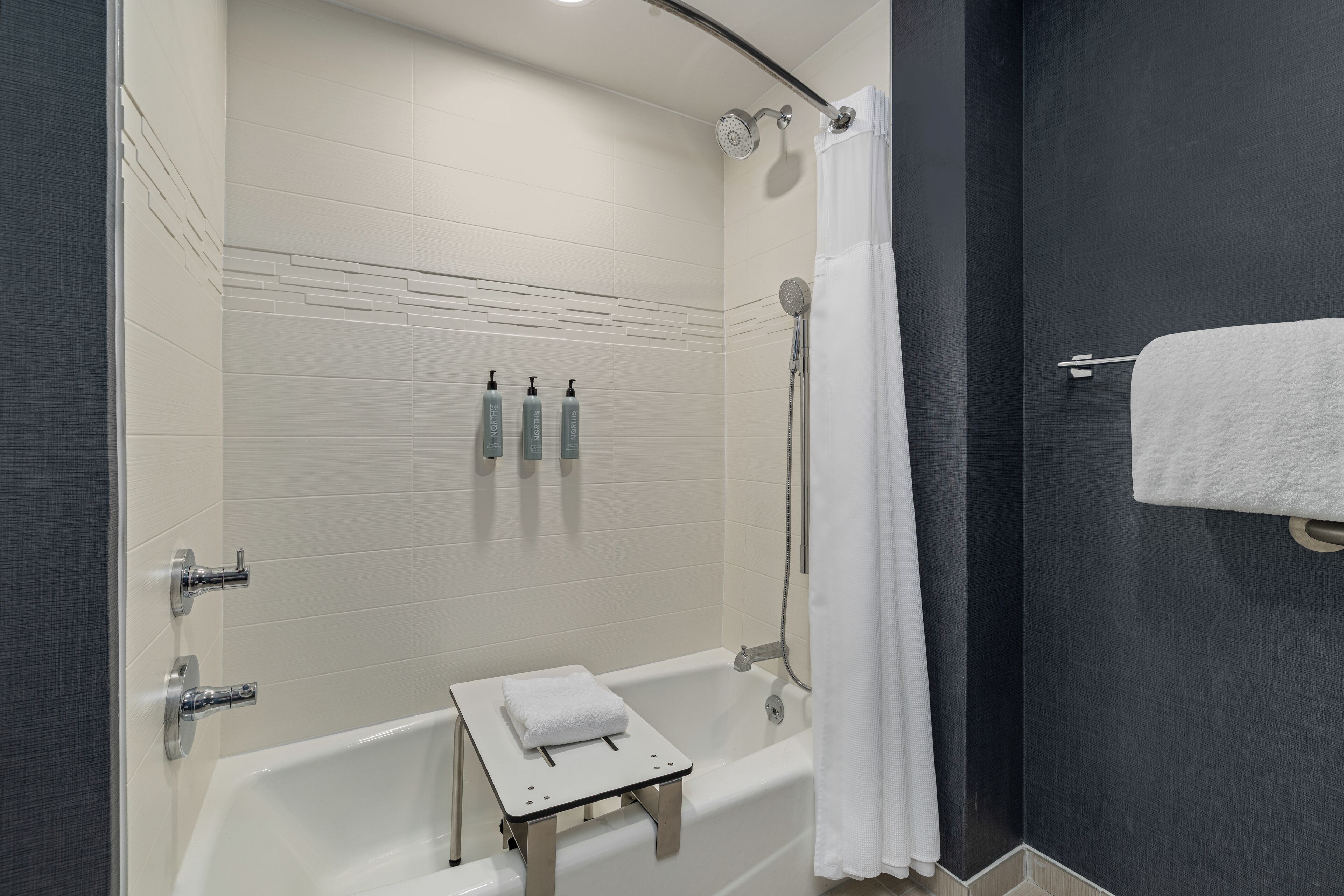 A modern bathroom with a bathtub, shower, and a small step stool with a towel.