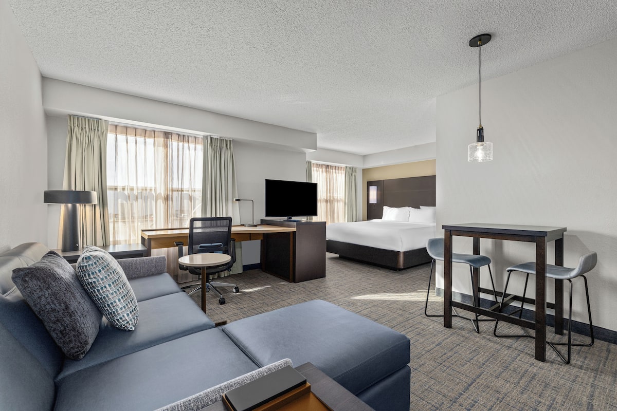A hotel room with a sofa, a desk, a bed, and a TV.
