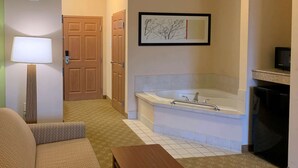 A hotel room with a sofa, a wooden table, a bathtub, and a framed picture on the wall. - Sleep Inn & Suites Gettysburg (Gettysburg)
