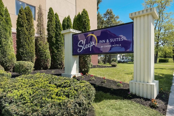 A sign for Sleep Inn & Suites by Choice Hotel with a landscaped garden in front.
