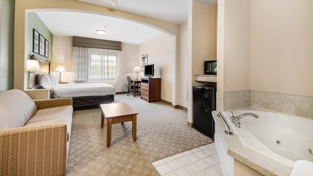 A hotel room with a bed, a sofa, a desk, a TV, a desk lamp, a coffee table, and a bathtub. - Sleep Inn & Suites Gettysburg (Gettysburg)