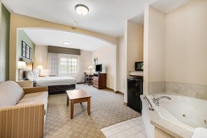 Une chambre d’hôtel comprenant un lit, un canapé, un bureau, une télévision, une lampe de bureau, une table basse et une baignoire.