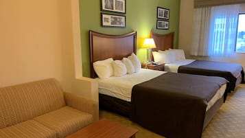 Een hotelkamer met twee bedden, een bank, een kleine tafel en een lamp. Er hangen ingelijste foto's aan de muur.