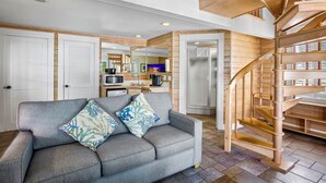 A spacious living area with a gray sofa, wooden staircase, and a kitchen in the background. - Eden House (Key West)