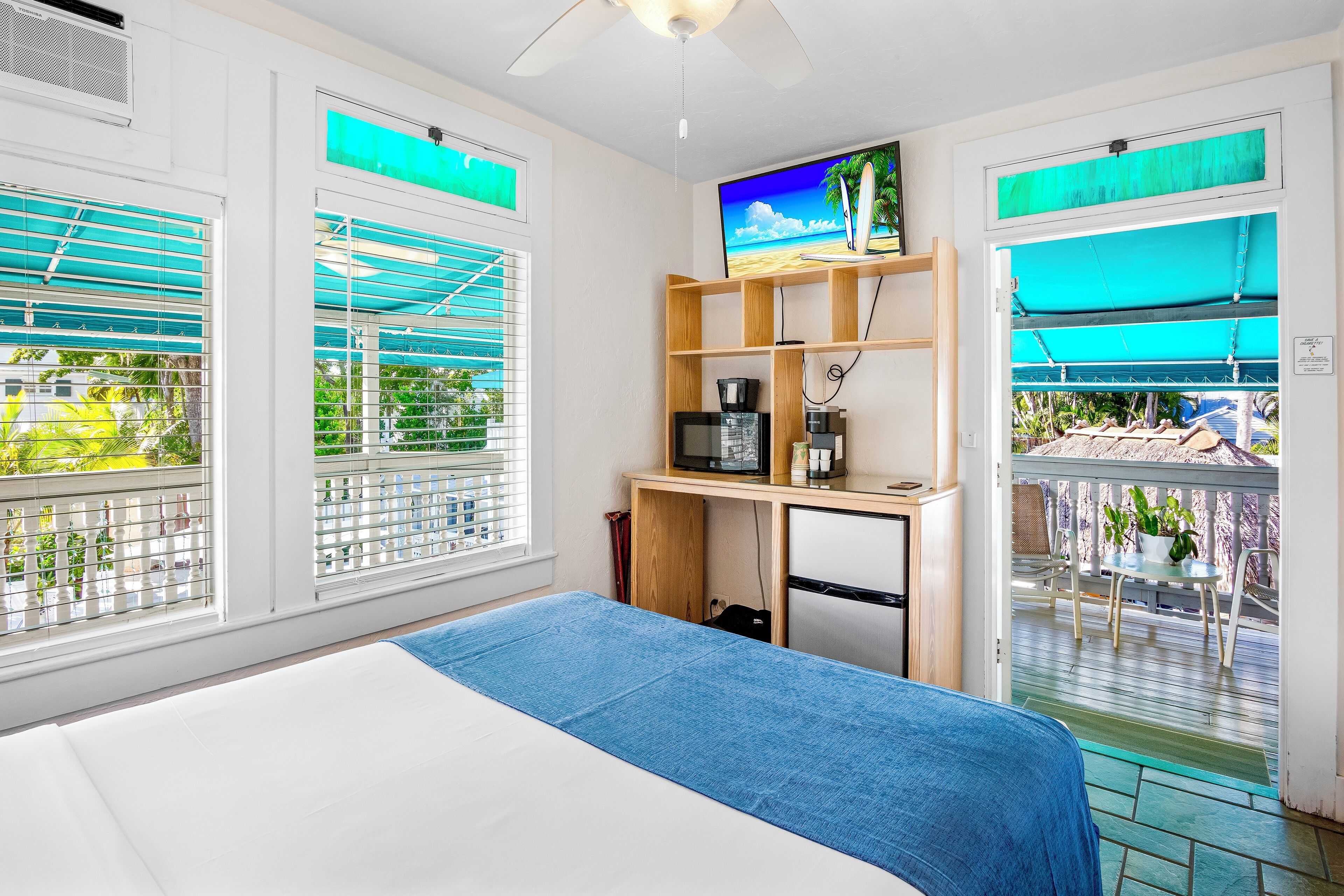 A hotel room with a bed, a desk with a TV, and a balcony with a view.
